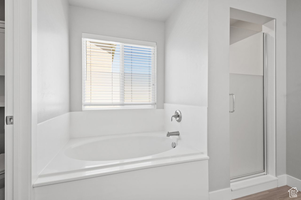 Bathroom with a bath, toilet, a stall shower, and wood finished floors