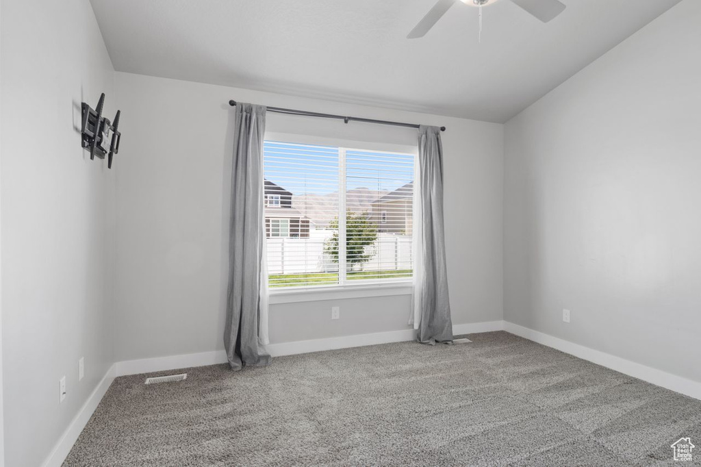 Carpeted empty room featuring ceiling fan, baseboards, and lofted ceiling