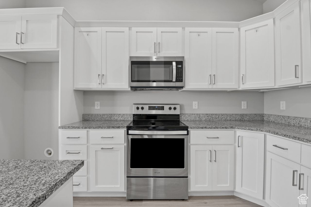 Kitchen featuring appliances with stainless steel finishes, white cabinetry, light wood finished floors, and light stone countertops