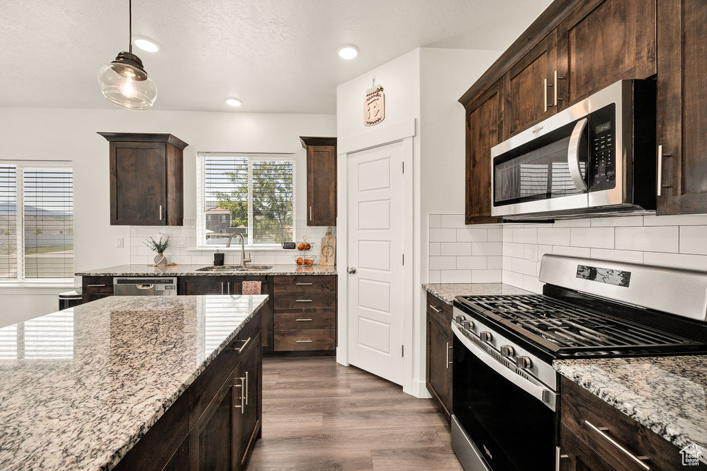 Kitchen with stainless steel appliances, a sink, dark brown cabinets, light stone counters, and recessed lighting