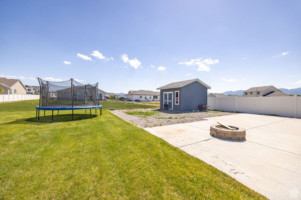 View of yard featuring an outdoor fire pit, a patio, a trampoline, and a residential view