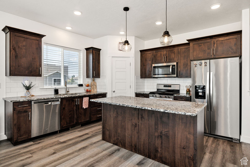 Kitchen with appliances with stainless steel finishes, a sink, a kitchen island, dark brown cabinetry, and decorative backsplash