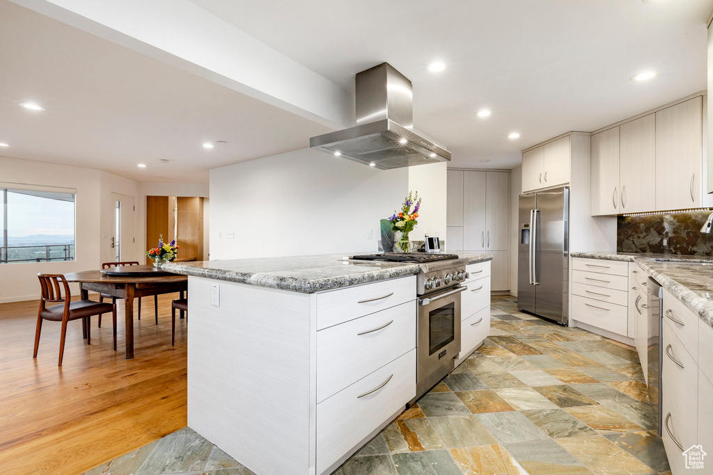 Kitchen with high quality appliances, island range hood, a sink, recessed lighting, and light stone counters