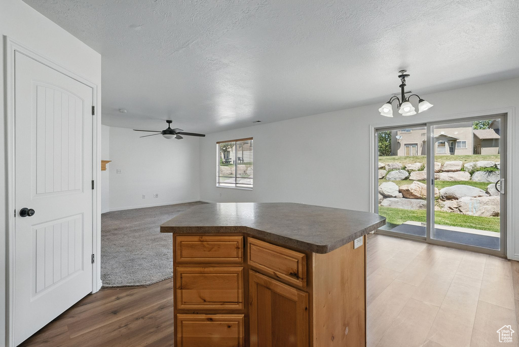 Kitchen featuring dark countertops, a chandelier, ceiling fan, a kitchen island, and pendant lighting