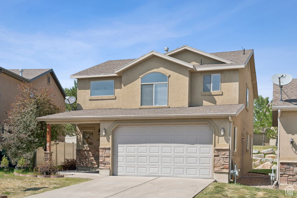 View of front of house featuring stone siding, a garage, driveway, and stucco siding