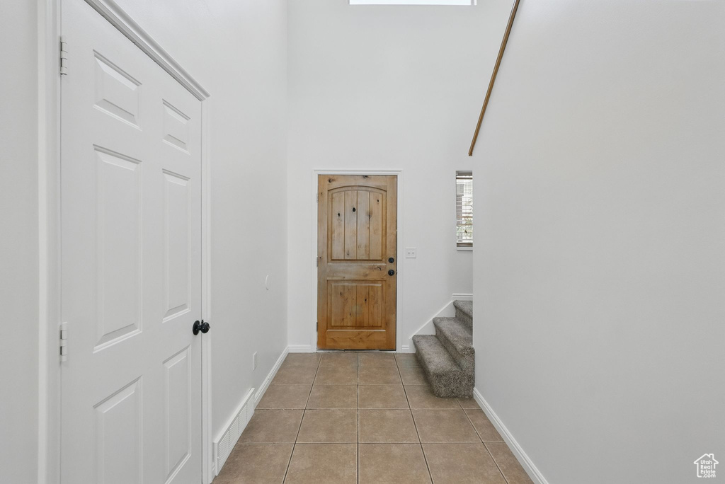 Foyer entrance featuring light tile patterned flooring, baseboards, a high ceiling, and stairs