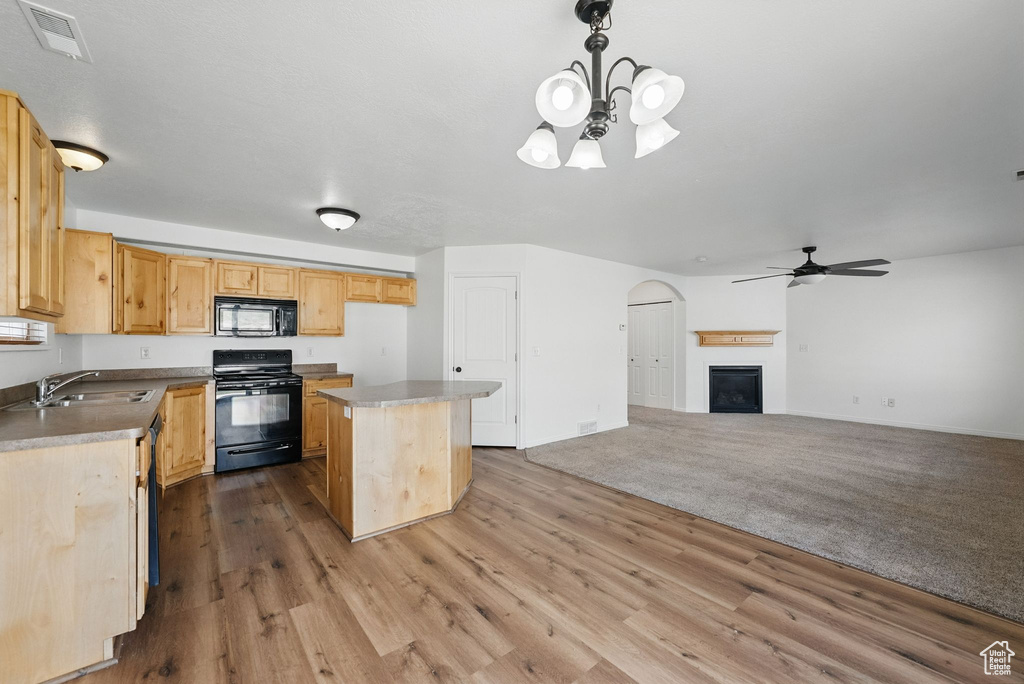 Kitchen with black appliances, a sink, a kitchen island, a chandelier, and wood finished floors