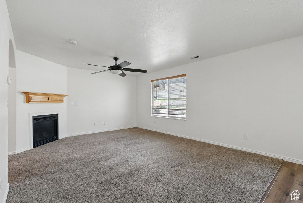 Unfurnished living room featuring a ceiling fan, a glass covered fireplace, baseboards, and carpet floors