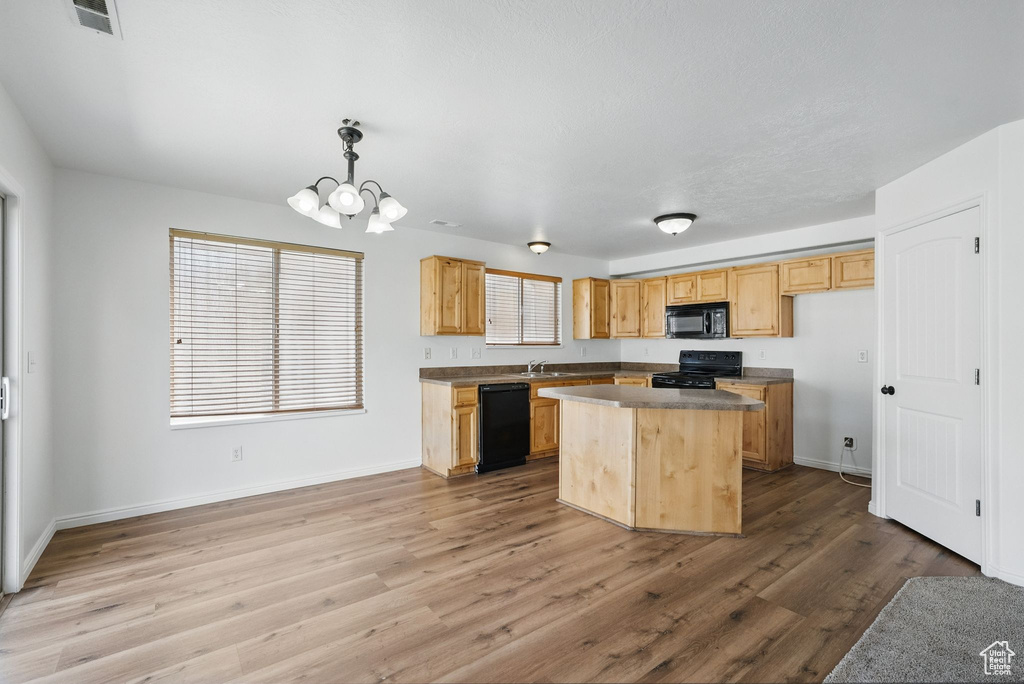 Kitchen featuring black appliances, a sink, a chandelier, wood finished floors, and a kitchen island