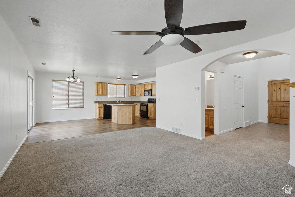 Unfurnished living room featuring carpet floors, arched walkways, a chandelier, a ceiling fan, and baseboards