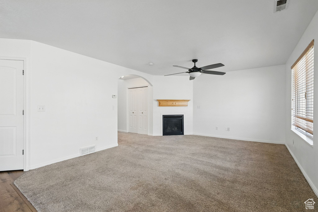 Unfurnished living room featuring a ceiling fan, arched walkways, a glass covered fireplace, baseboards, and carpet floors