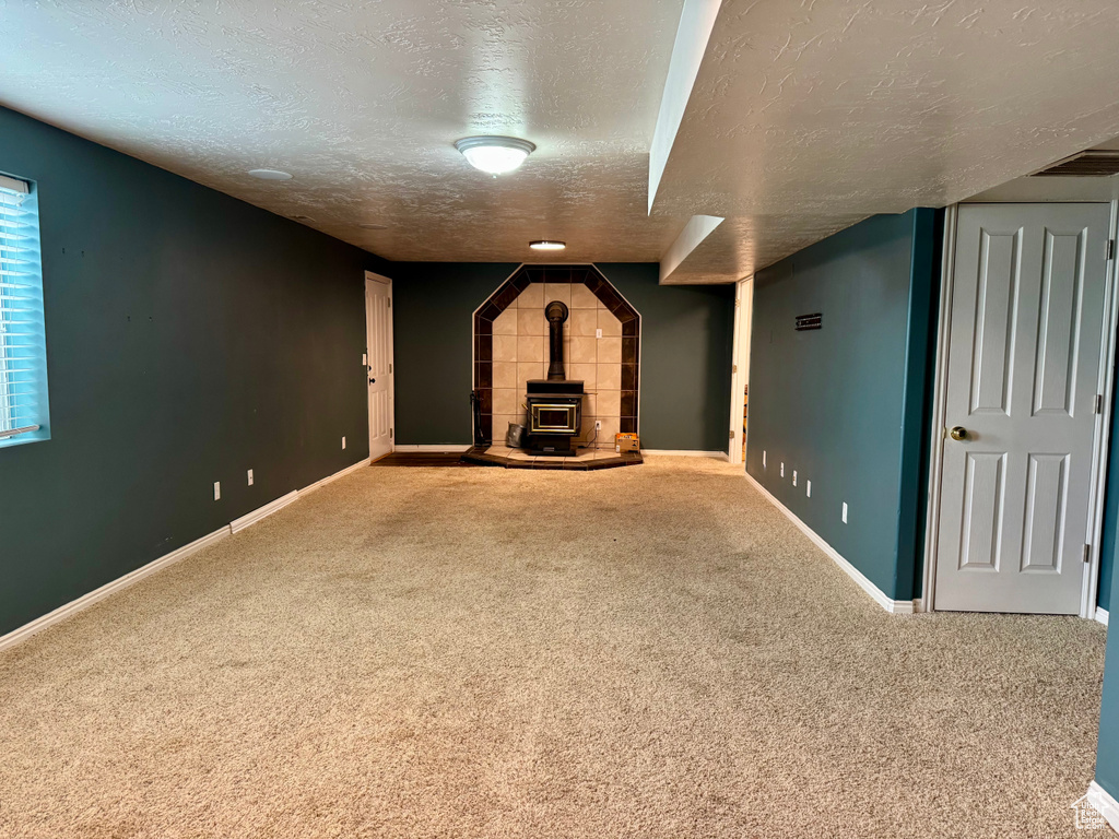Unfurnished living room with a textured ceiling, a wood stove, carpet, and baseboards