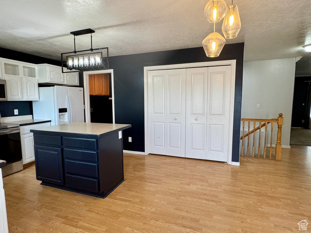 Kitchen with stainless steel appliances, white cabinetry, light wood finished floors, a textured ceiling, and a center island