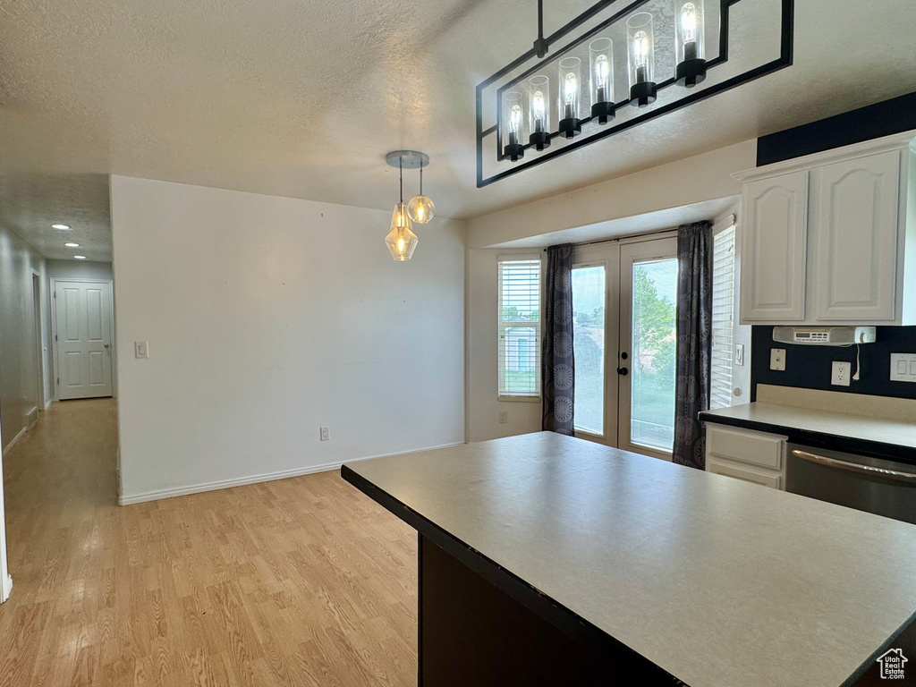 Kitchen with french doors, white cabinets, light wood-style floors, stainless steel dishwasher, and pendant lighting