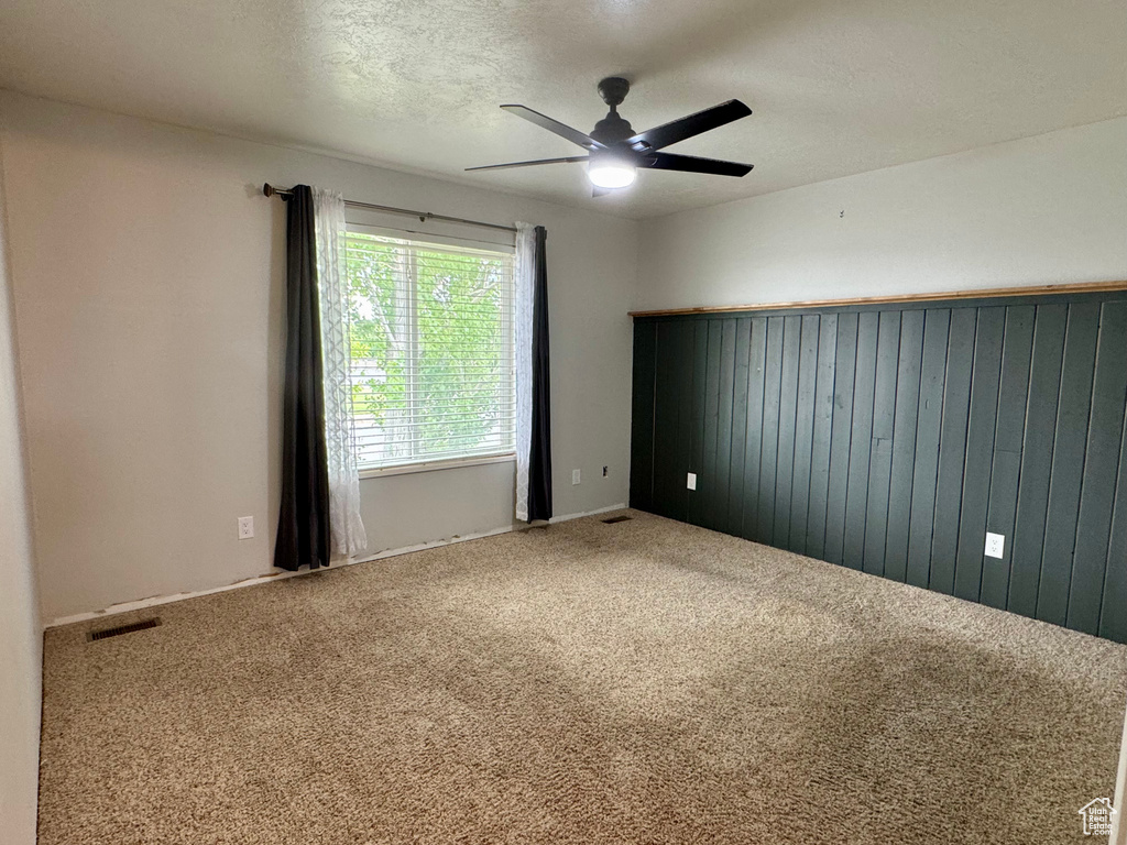 Empty room with carpet, ceiling fan, wood walls, and a textured ceiling