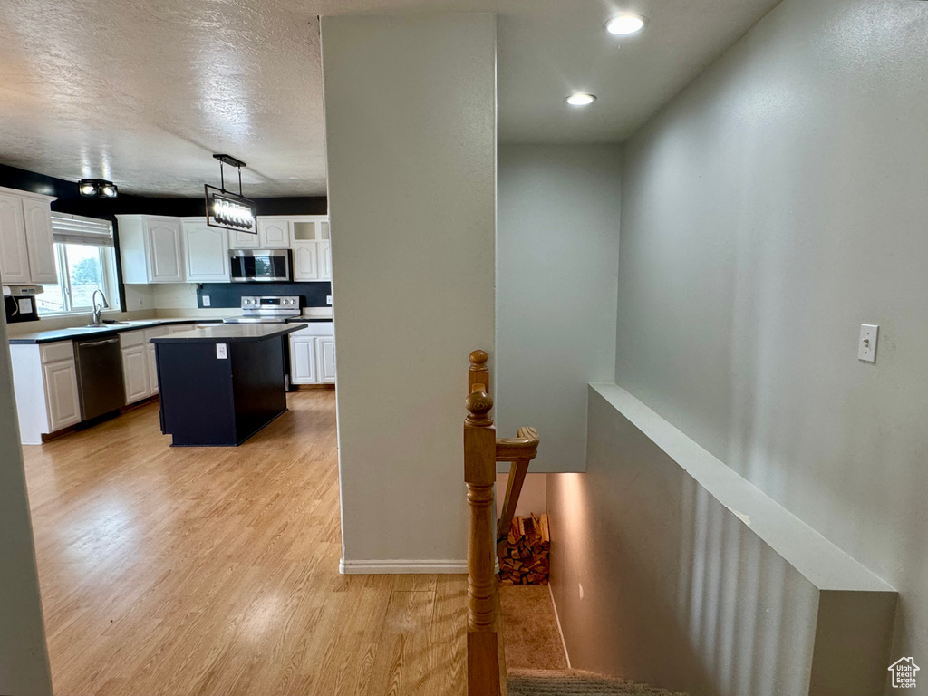 Kitchen featuring stainless steel appliances, a sink, white cabinets, a kitchen island, and light wood-style floors