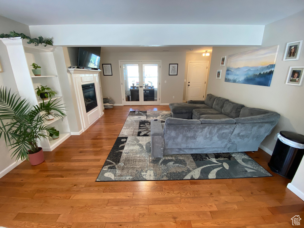Living room featuring wood finished floors, french doors, a glass covered fireplace, and baseboards