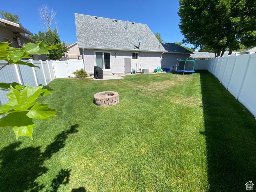 Back of house featuring a fire pit, a trampoline, stucco siding, roof with shingles, and central air condition unit