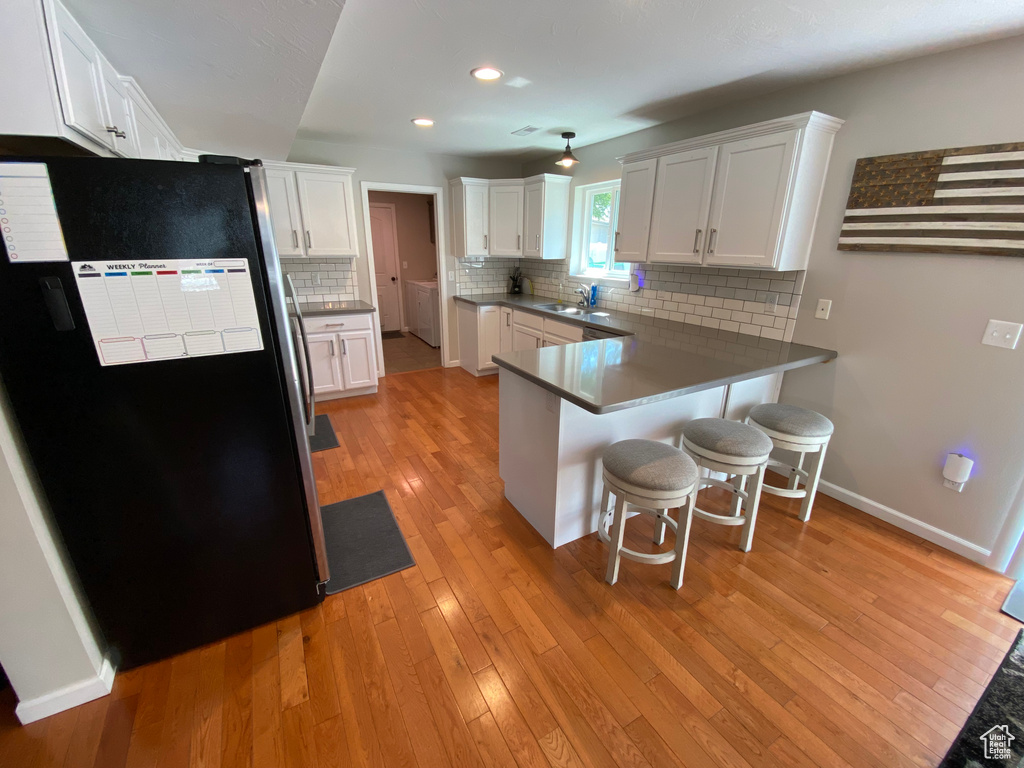Kitchen with freestanding refrigerator, a peninsula, a kitchen bar, light wood finished floors, and a sink