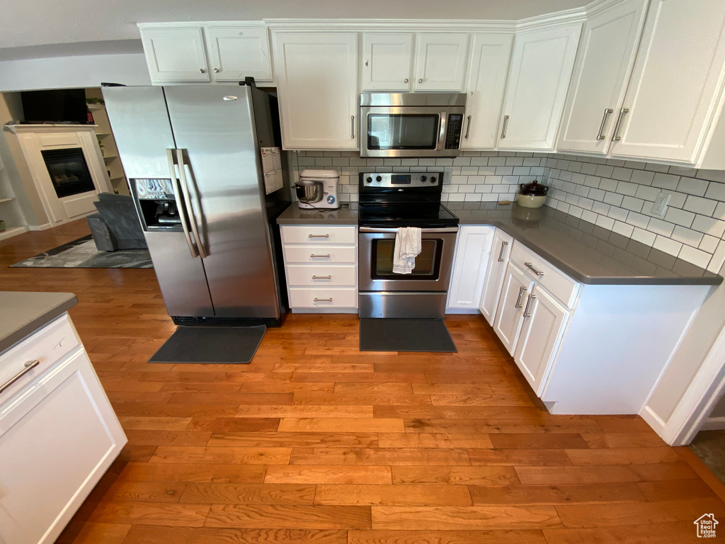 Kitchen with appliances with stainless steel finishes, light wood finished floors, dark countertops, and white cabinetry
