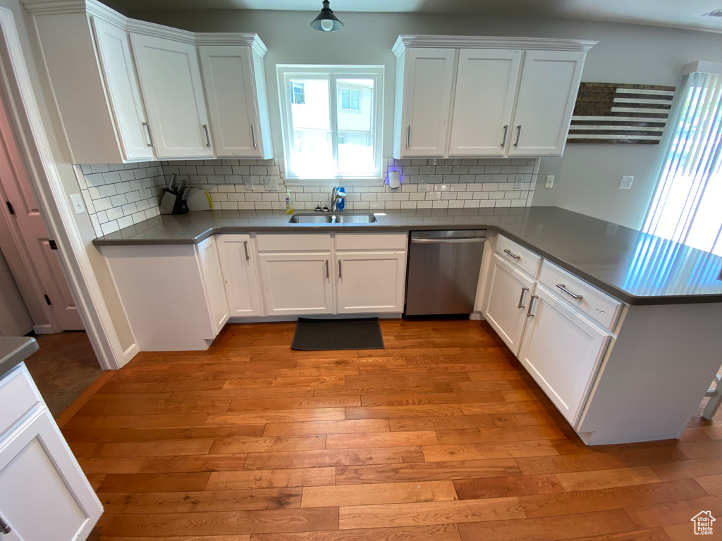 Kitchen featuring stainless steel dishwasher, a sink, a peninsula, light wood-style flooring, and white cabinetry