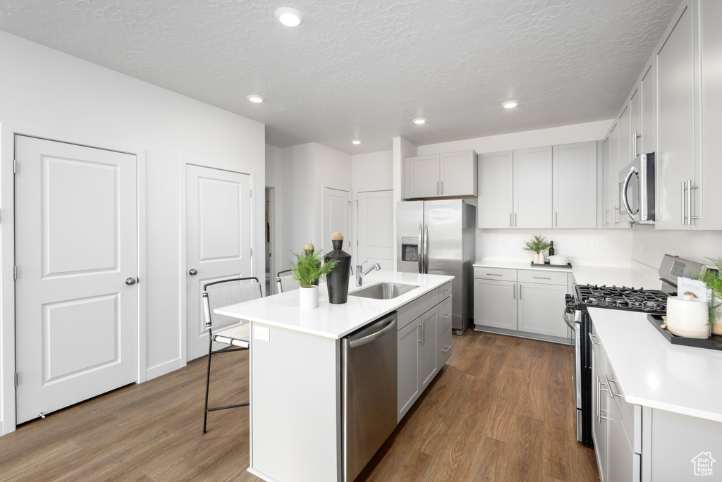 Kitchen featuring appliances with stainless steel finishes, a breakfast bar, wood finished floors, a textured ceiling, and recessed lighting