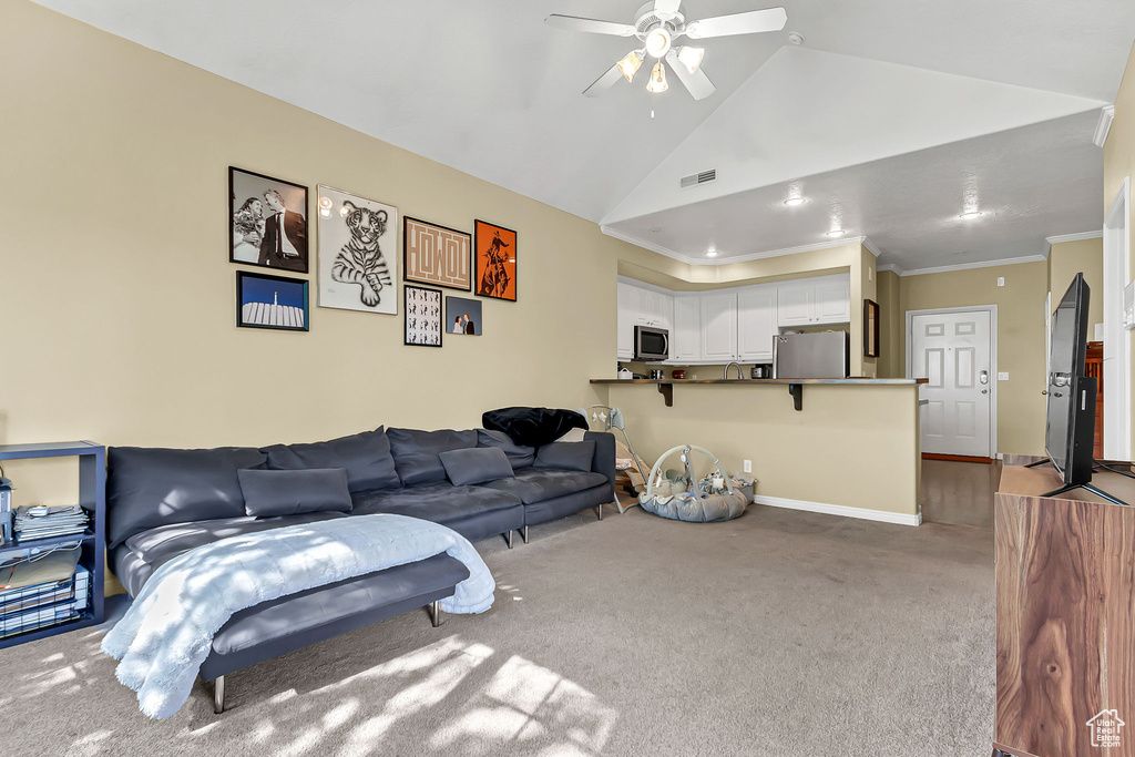 Living room with carpet floors, a ceiling fan, baseboards, lofted ceiling, and ornamental molding