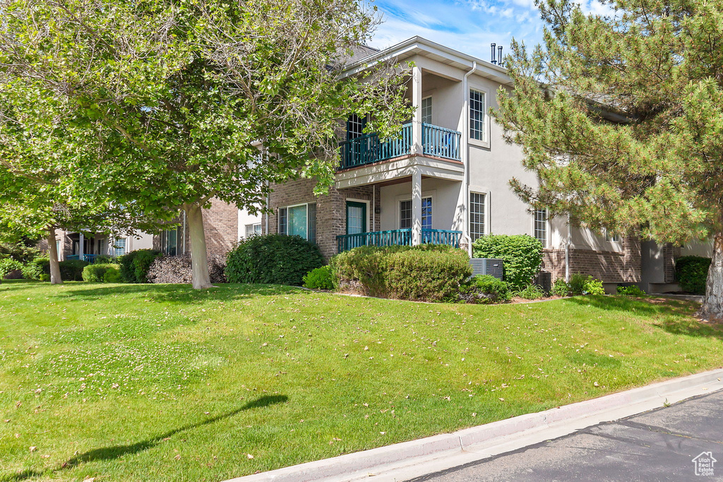 View of front of property with a balcony, stucco siding, brick siding, and a front lawn