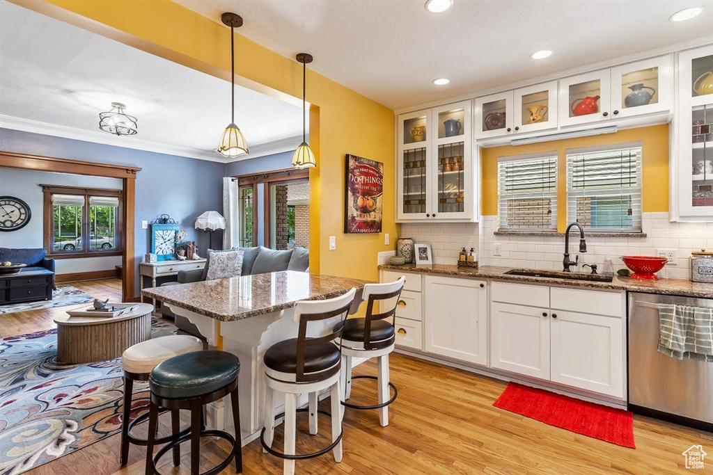 Kitchen featuring stainless steel dishwasher, a sink, white cabinetry, light stone counters, and tasteful backsplash