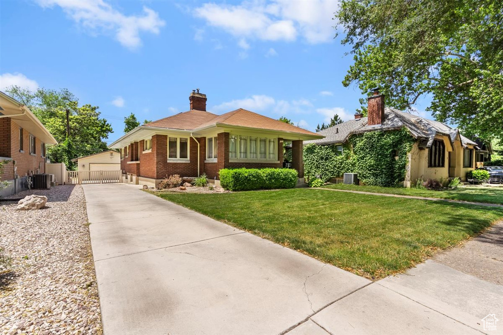 View of front of property with an outdoor structure, brick siding, a front lawn, a chimney, and central AC