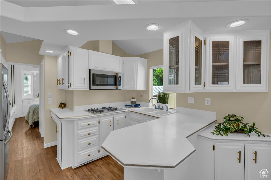 Kitchen featuring stainless steel appliances, a sink, a peninsula, light countertops, and lofted ceiling