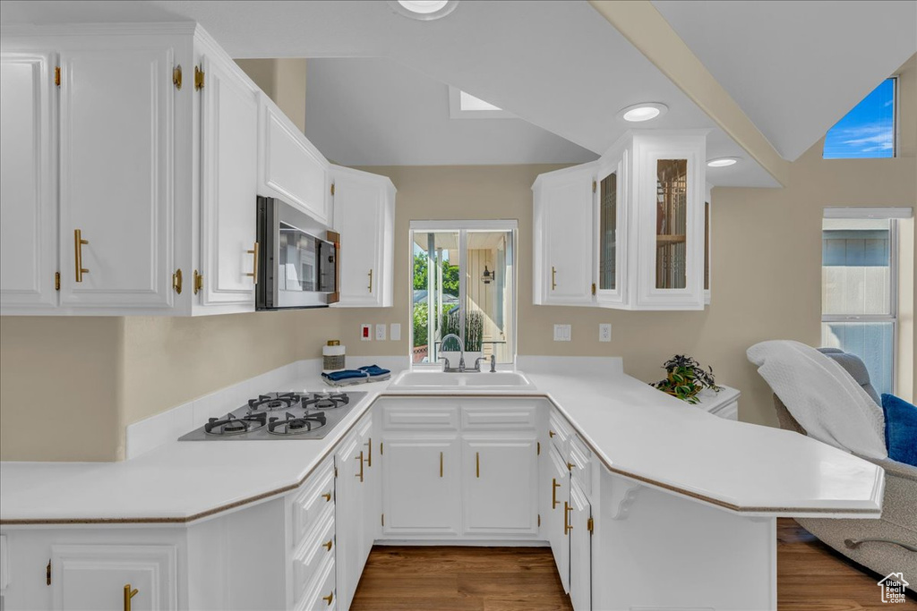 Kitchen featuring stainless steel microwave, a sink, a peninsula, white gas cooktop, and vaulted ceiling