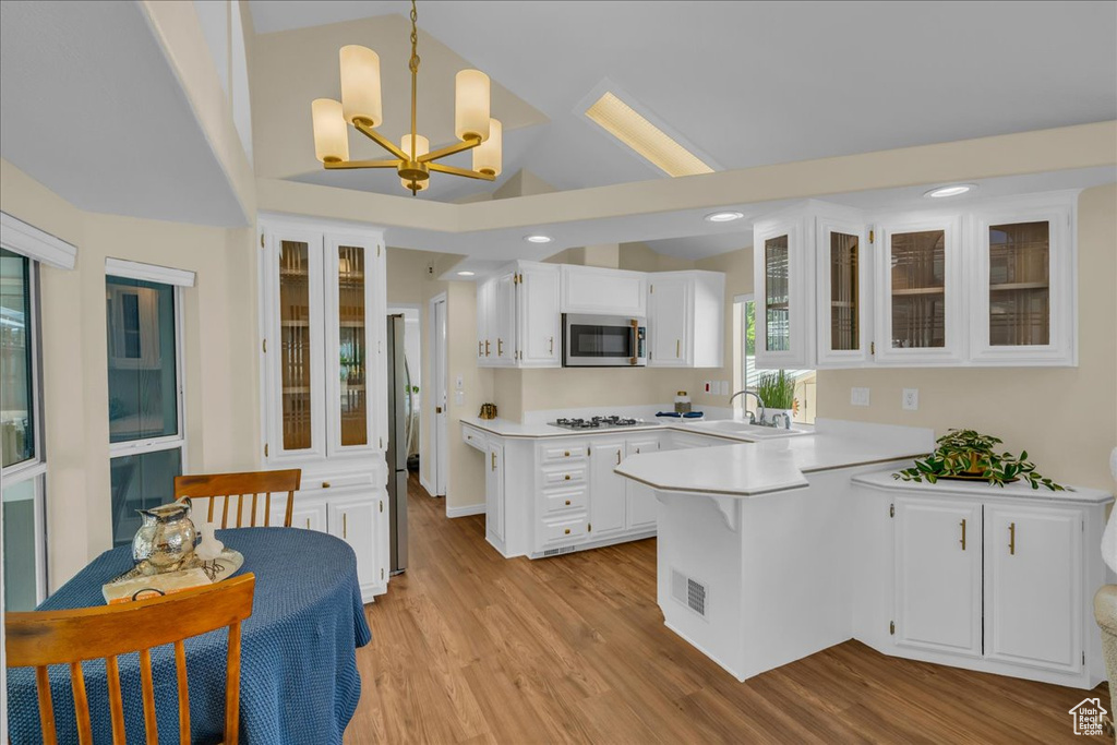 Kitchen featuring stainless steel microwave, a peninsula, white gas cooktop, light countertops, and white cabinetry