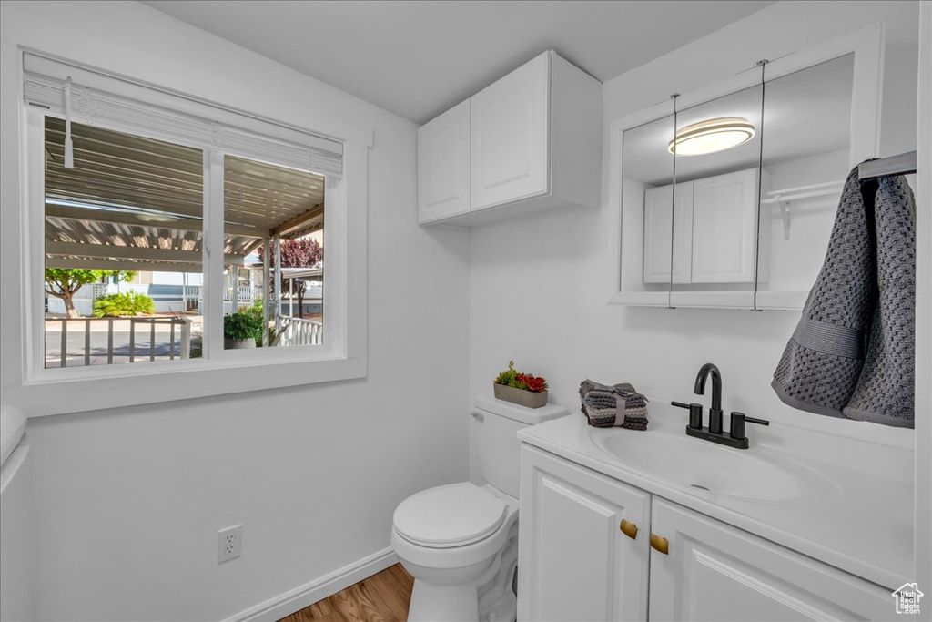 Half bathroom featuring vanity, toilet, wood finished floors, and baseboards