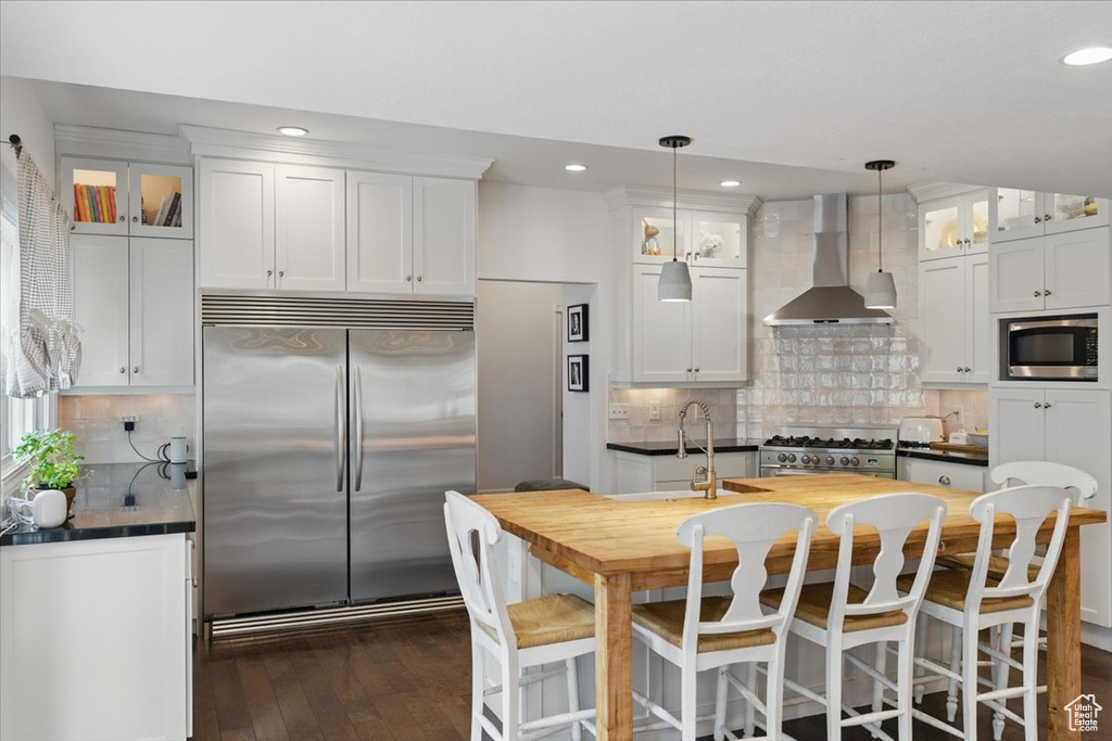 Kitchen featuring built in appliances, wall chimney exhaust hood, a sink, backsplash, and recessed lighting