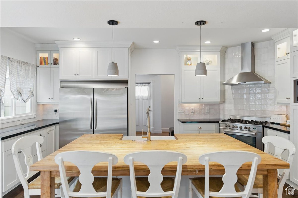Kitchen featuring wall chimney exhaust hood, stainless steel appliances, dark countertops, a sink, and white cabinets
