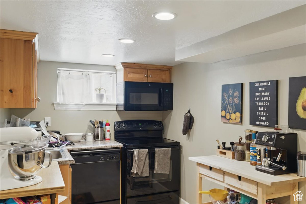 Kitchen with black appliances, light countertops, brown cabinetry, and a textured ceiling