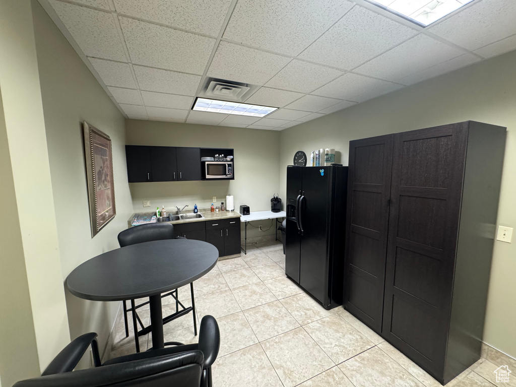 Kitchen featuring black fridge with ice dispenser, stainless steel microwave, a paneled ceiling, light countertops, and dark cabinetry