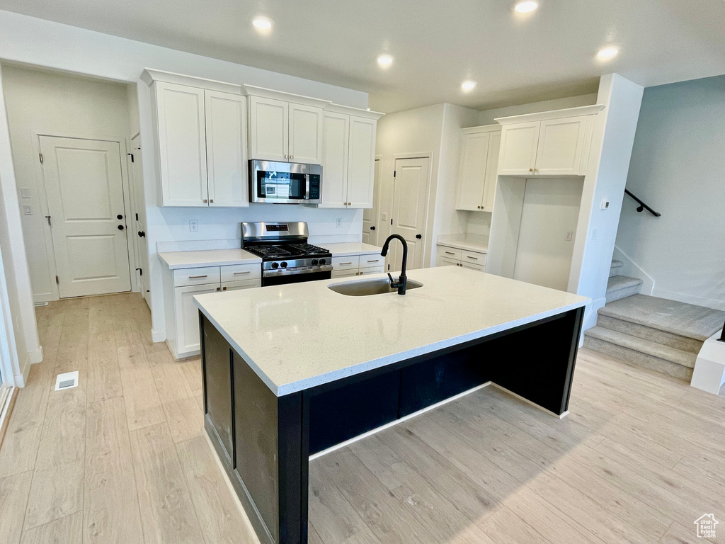 Kitchen with stainless steel appliances, an island with sink, light wood finished floors, white cabinets, and recessed lighting