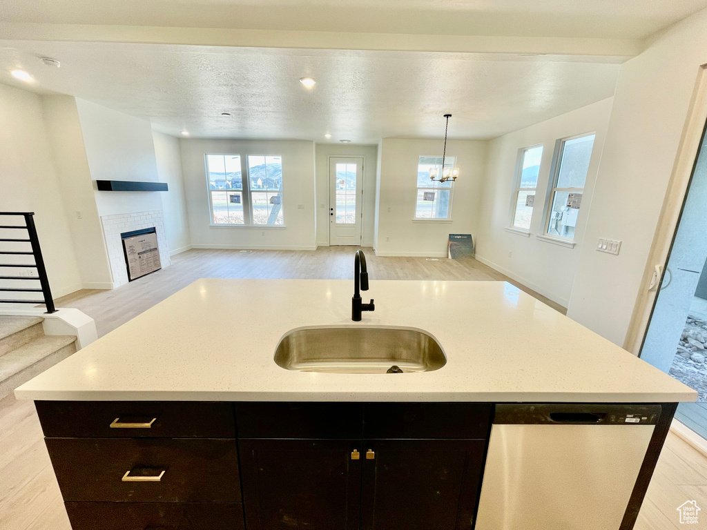 Kitchen featuring dishwasher, open floor plan, light wood-style flooring, a kitchen island with sink, and a tiled fireplace