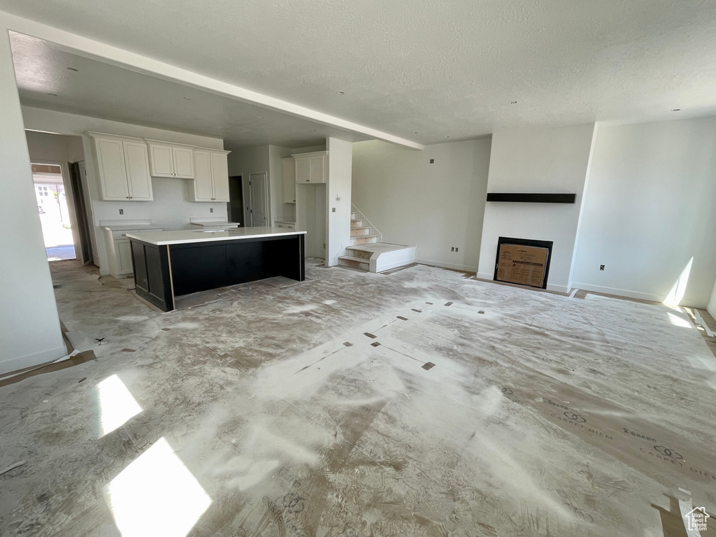 Kitchen featuring white cabinets, a fireplace, a textured ceiling, a center island, and baseboards