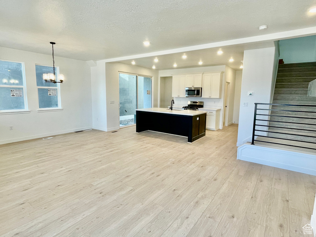 Kitchen with appliances with stainless steel finishes, a kitchen island with sink, a chandelier, light countertops, and open floor plan