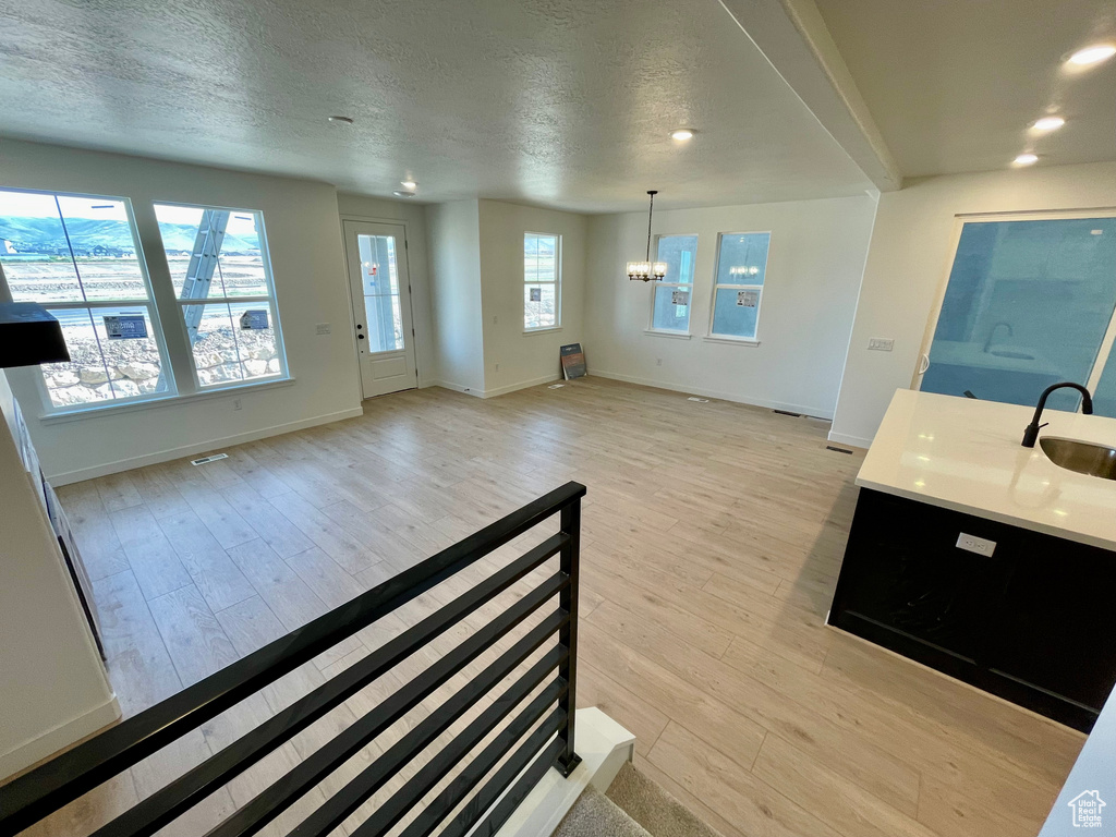 Unfurnished living room featuring a chandelier, light wood-type flooring, a textured ceiling, and recessed lighting
