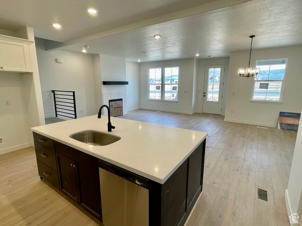 Kitchen featuring dishwasher, a tiled fireplace, light wood finished floors, light countertops, and open floor plan