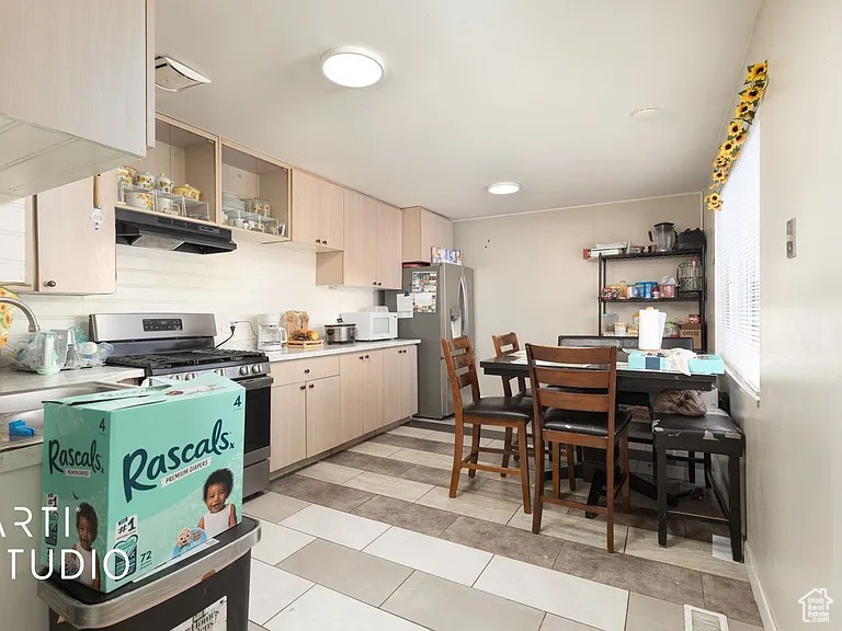 Kitchen with appliances with stainless steel finishes, light countertops, open shelves, under cabinet range hood, and light tile patterned floors