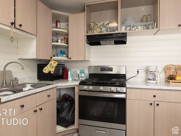 Kitchen featuring stainless steel gas stove, ventilation hood, and light brown cabinetry