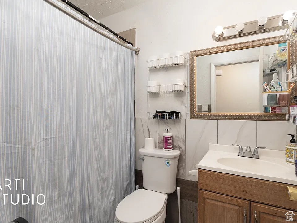 Full bath with vanity, toilet, a shower with shower curtain, and tile walls