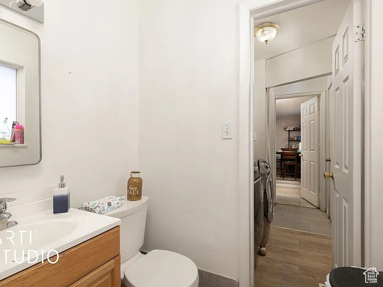 Half bath with washing machine and clothes dryer, toilet, vanity, and wood finished floors