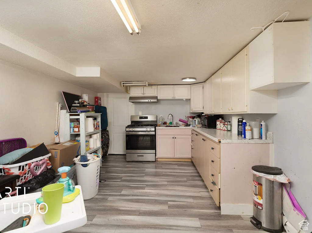 Kitchen with stainless steel range with gas stovetop, under cabinet range hood, light countertops, white cabinets, and light wood-style flooring
