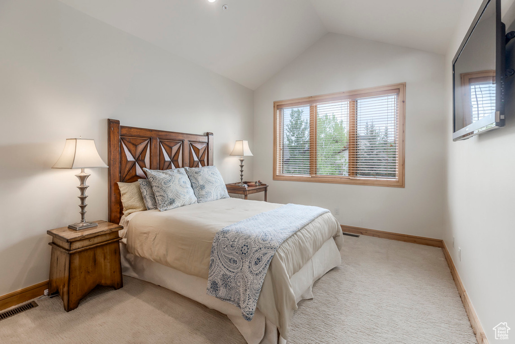 Bedroom with light colored carpet, multiple windows, baseboards, and lofted ceiling